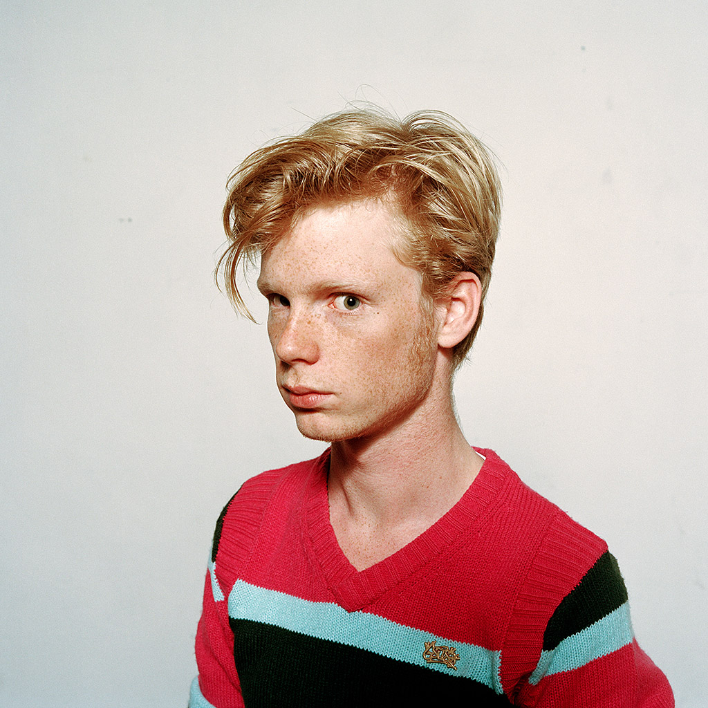 You see Eric Schrijver, wearing a pink sweater. This picture shows a three-quarter profile; Eric looks into the camera, serious and somewhat formal. You can make out from the lighting and the sharpness of the image that it was probably taken in a studio.